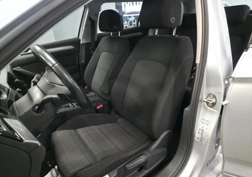 Vue intérieure côté conducteur d'une Volkswagen Passat SW 2021 gris, sièges tissu noir à motifs et volant cuir.