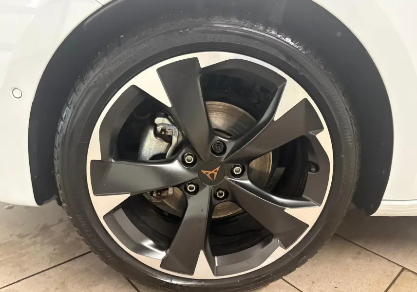 Gros plan sur la roue avant droite d'une CUPRA Leon blanche Nevada avec jante alliage noire et argentée au design sportif.