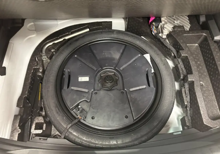 Vue rapprochée du pneu de secours noir dans le coffre d'une CUPRA Leon blanc Nevada 2024.