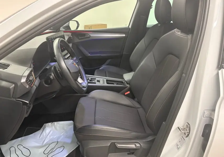 Intérieur avant droit de la CUPRA Leon blanc Nevada 2024, sièges noirs avec surpiqûres et volant multifonction.