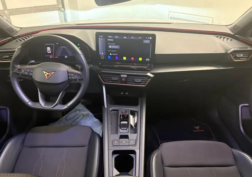 Vue intérieure frontale du tableau de bord et volant noir de la CUPRA Leon 2024 avec écran tactile central allumé.