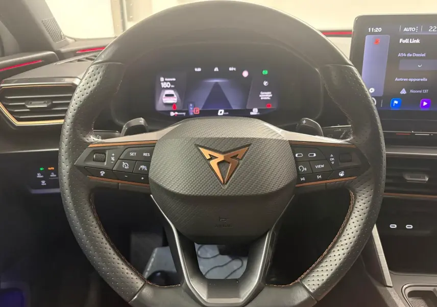 Vue centrée sur le volant perforé noir avec logo CUPRA cuivré, tableau de bord numérique et écran tactile intérieur.