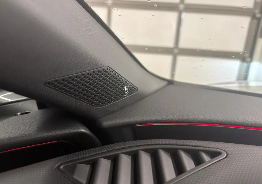 Détail intérieur côté gauche du tableau de bord de la CUPRA Leon 2024 avec haut-parleur Beats et éclairage d'ambiance rouge.