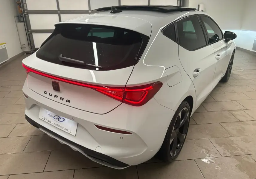 Vue 3/4 arrière droite d'une CUPRA Leon blanche Nevada avec toit ouvrant panoramique dans un garage.