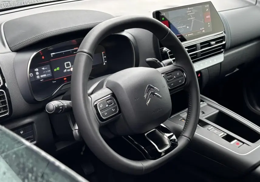 Intérieur du Citroën C5 Aircross 2025 vu côté conducteur, volant cuir noir et tableau de bord numérique avec écran tactile.