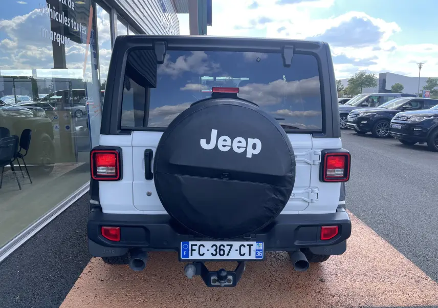 Vue arrière d'un Jeep Wrangler blanc de 2018 avec roue de secours couverte et feux carrés rouges.