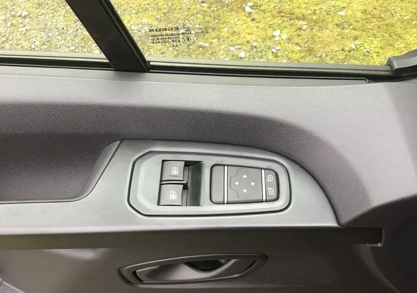 Vue rapprochée des commandes de lève-vitres et réglage des rétroviseurs sur la porte côté conducteur du Renault Trafic Fourgon noir 2025.