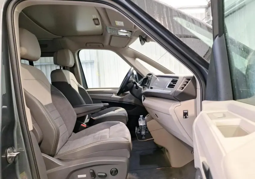 Intérieur côté conducteur du Volkswagen California T7 gris Indium, sièges ErgoComfort bicolores avec accoudoirs et tableau de bord clair.