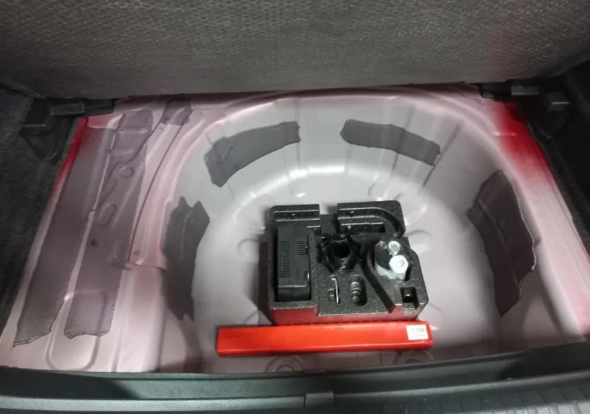 Coffre ouvert montrant la zone de rangement sous plancher avec outils et peinture rouge Désir visible sur la carrosserie.