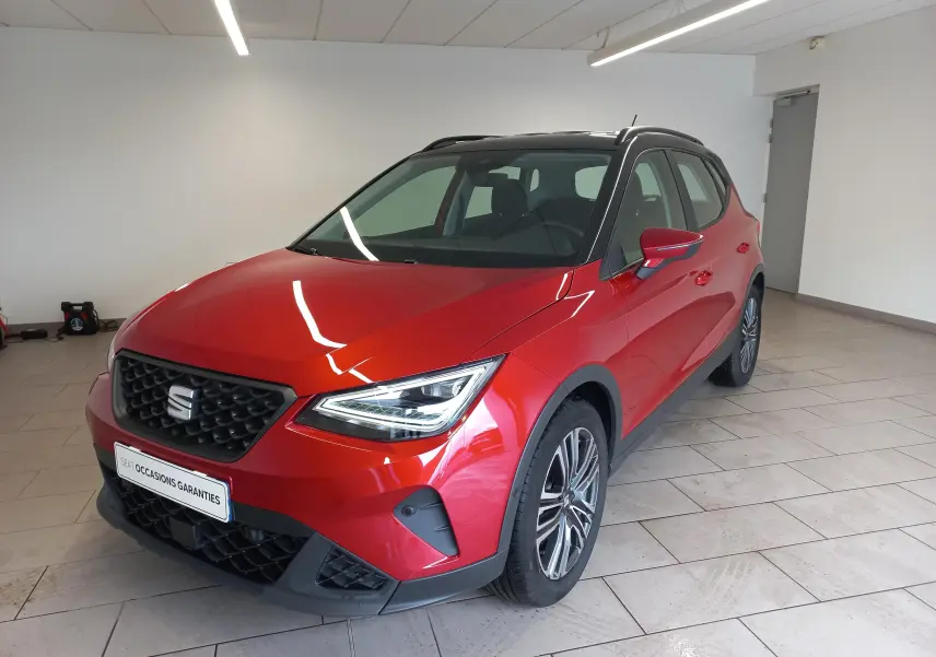 Vue 3/4 avant droite du SEAT Arona rouge Désir avec toit noir Minuit, en intérieur, soulignant ses phares LED et jantes alliage.