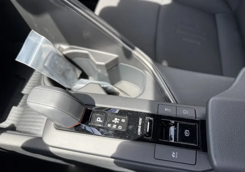 Gros plan sur la console centrale du Toyota C-HR 1.8 Hybride 2025, avec levier de vitesse et boutons de mode de conduite.