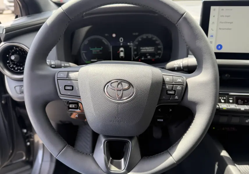 Vue rapprochée du volant noir du Toyota C-HR 1.8 Hybride 140 Style 2025 avec commandes intégrées et tableau de bord numérique.