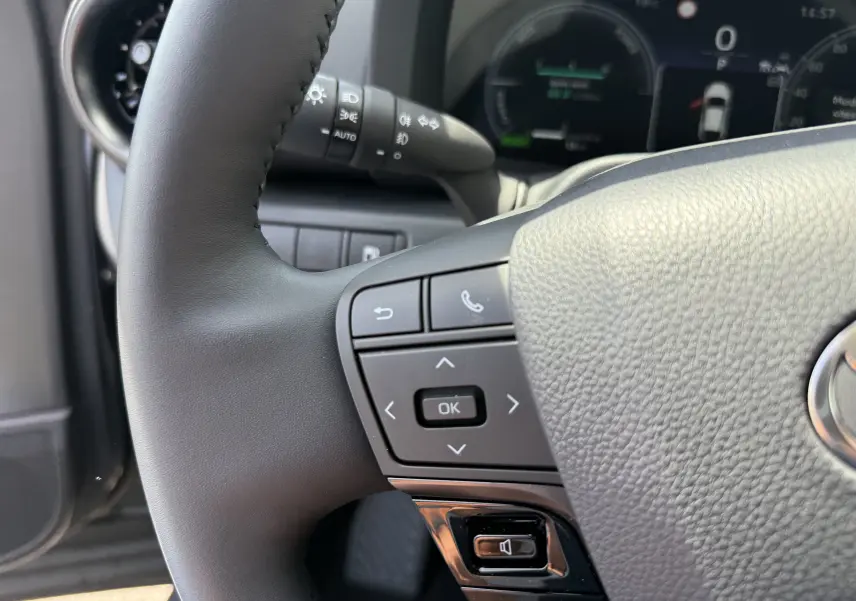 Gros plan sur le volant noir du Toyota C-HR 1.8 Hybride 140 Style 2025 avec commandes intégrées et tableau de bord numérique flou.