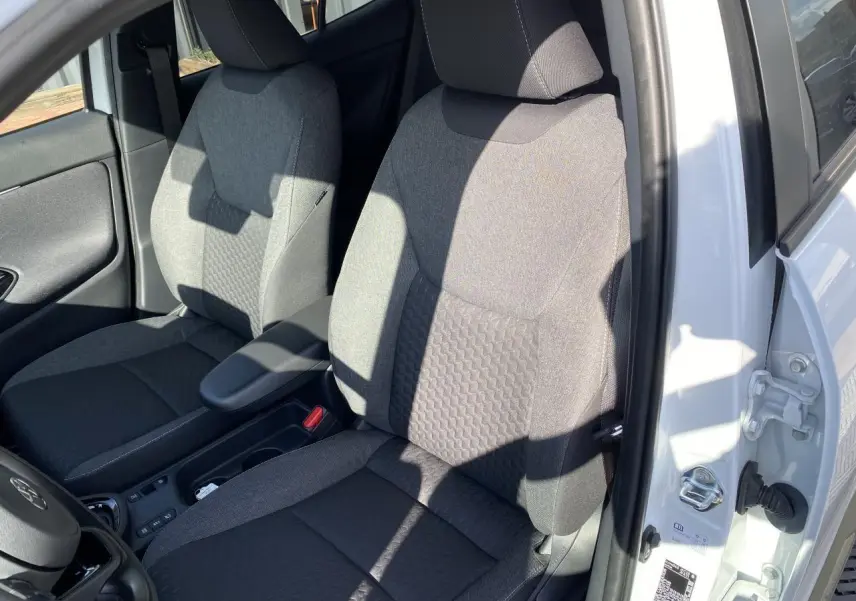 Vue rapprochée des sièges avant gris tissu du Toyota Yaris Cross blanc, avec accoudoir central et portière ouverte côté gauche.