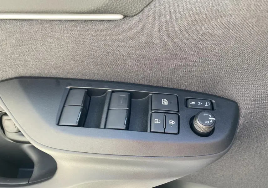 Gros plan sur les commandes de lève-vitres et réglages des rétroviseurs côté conducteur d'une Toyota Yaris Cross blanche.