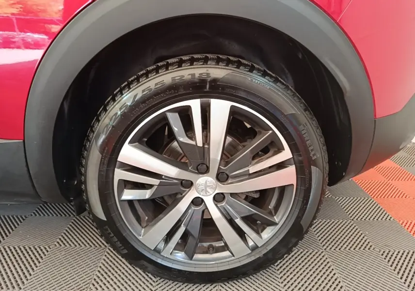 Gros plan sur la roue avant droite du Peugeot 3008 rouge, mettant en valeur la jante alliage bicolore et le pneu Pirelli.