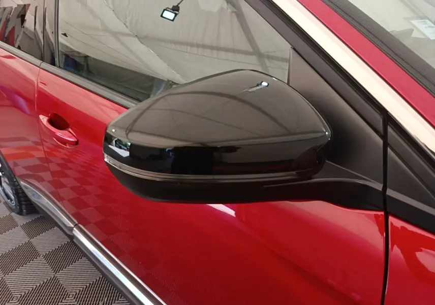 Gros plan sur le rétroviseur noir côté conducteur d’un Peugeot 3008 rouge, avec poignée de porte visible.