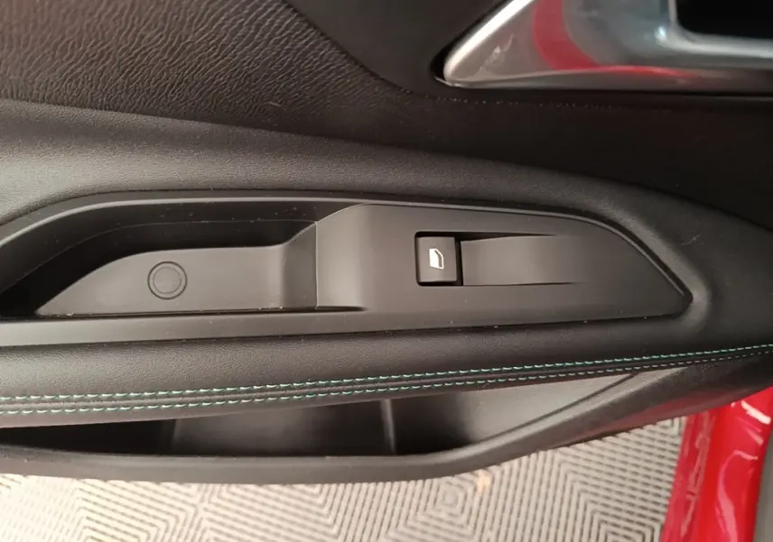 Détail de la poignée intérieure côté conducteur du Peugeot 3008 rouge avec couture bleue sur la garniture de porte noire.