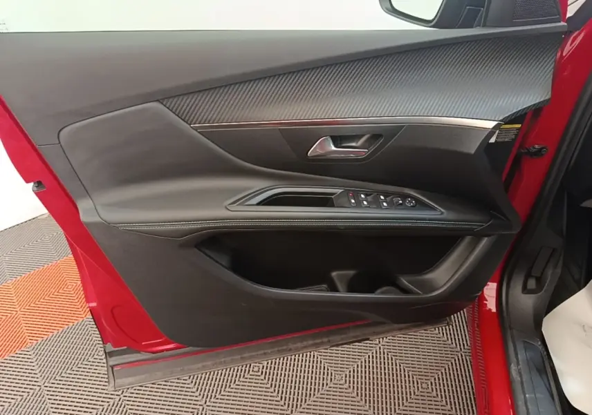 Vue intérieure côté gauche de la porte avant rouge du Peugeot 3008 avec garniture noire et commandes électriques.