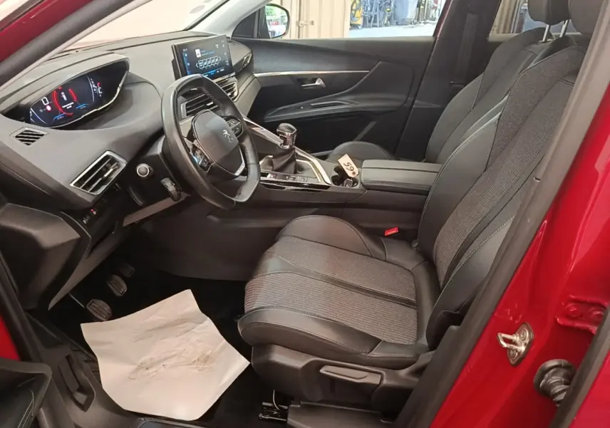 Vue intérieure côté conducteur d'un Peugeot 3008 rouge, avec tableau de bord numérique et sièges tissu-cuir noirs.