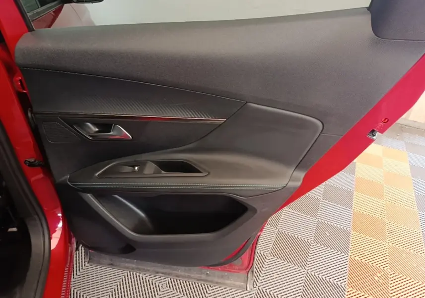 Vue rapprochée de la porte avant gauche rouge du Peugeot 3008, avec garniture noire et poignée métallique.