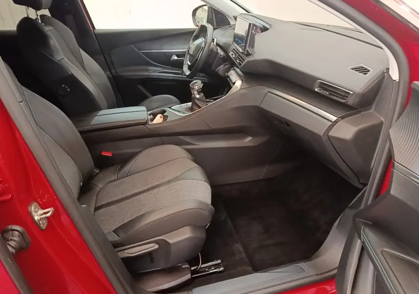 Vue intérieure côté passager avant d’un Peugeot 3008 rouge, sièges tissu et cuir noir, tableau de bord moderne avec écran tactile.