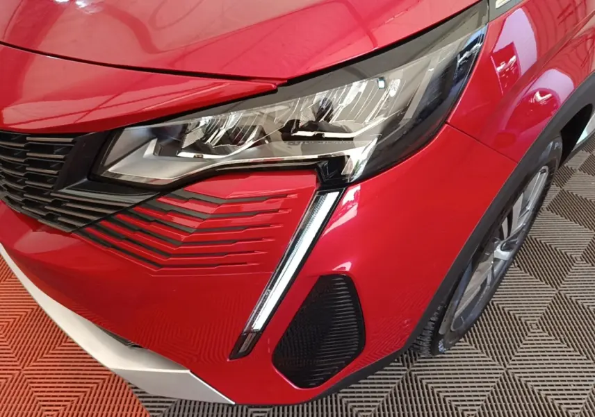 Gros plan sur l’avant droit rouge vif du Peugeot 3008, mettant en valeur le phare LED et la calandre noire.