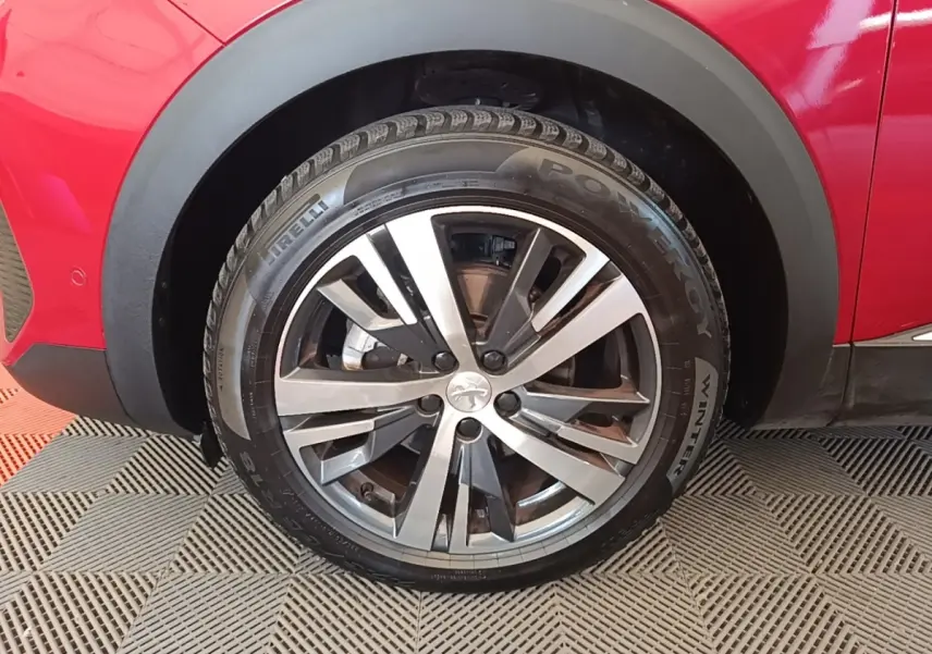 Gros plan sur la roue avant gauche du Peugeot 3008 rouge, jante alliage bicolore et pneu hiver Pirelli.