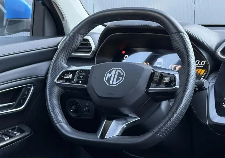 Vue rapprochée du volant en cuir noir perforé du MG ZS 1.5 Hybrid+ 197 Luxury avec tableau de bord numérique.