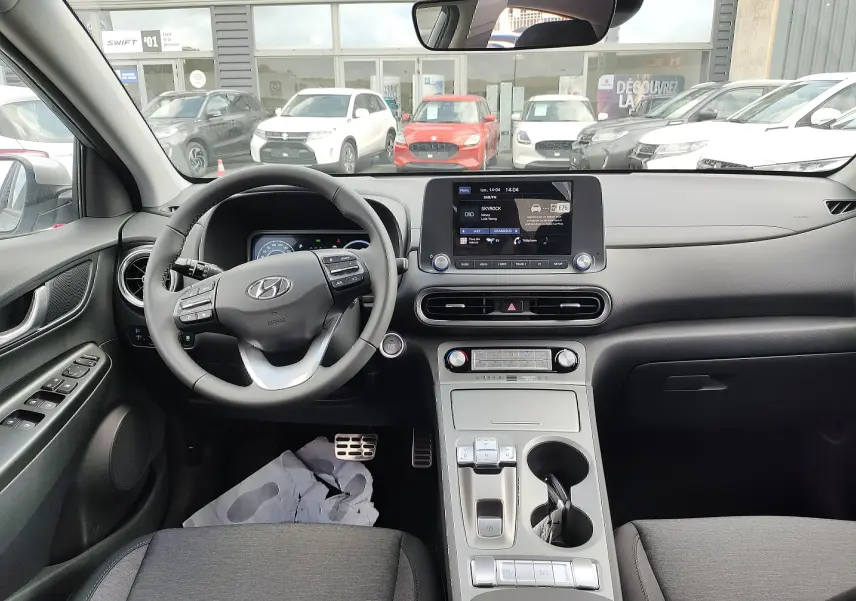Vue intérieure du tableau de bord et volant cuir noir du Hyundai Kona Electric 2025, avec écran tactile central et commandes au volant.