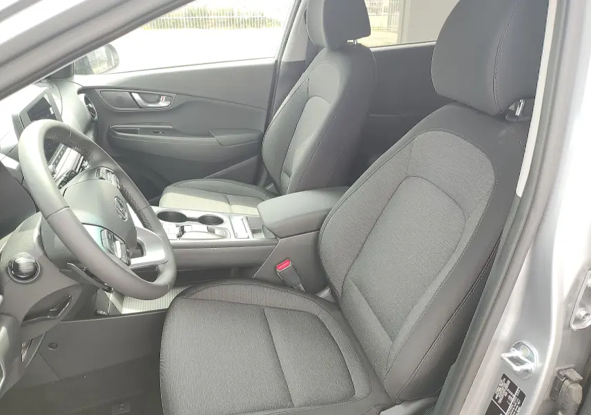 Intérieur avant du Hyundai Kona Electric 2025, sièges noirs en tissu et console centrale vue côté conducteur.
