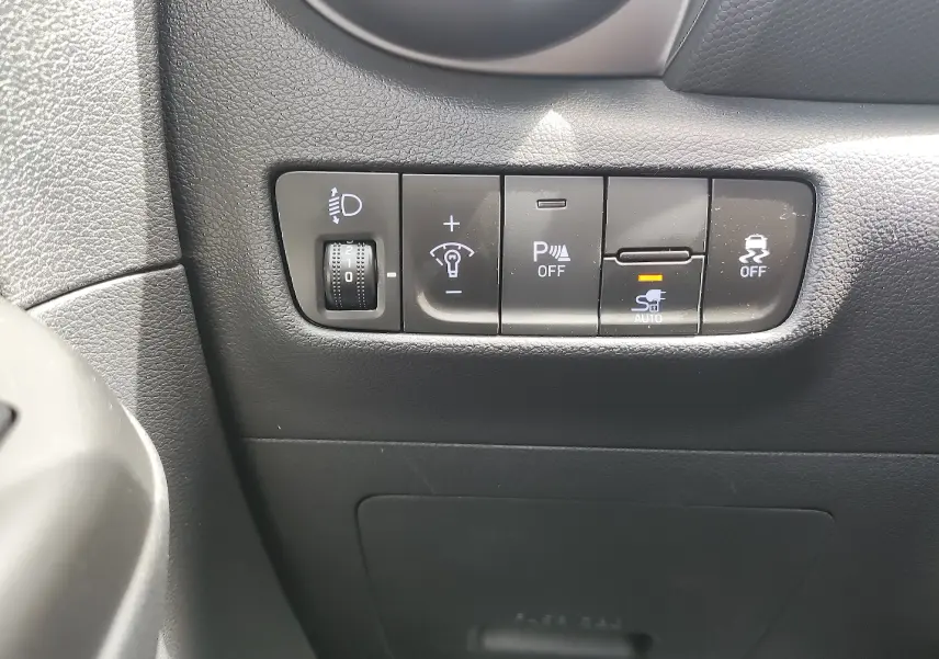 Vue rapprochée des commandes de réglage des phares et aides à la conduite sur le tableau de bord noir du Hyundai Kona électrique gris.