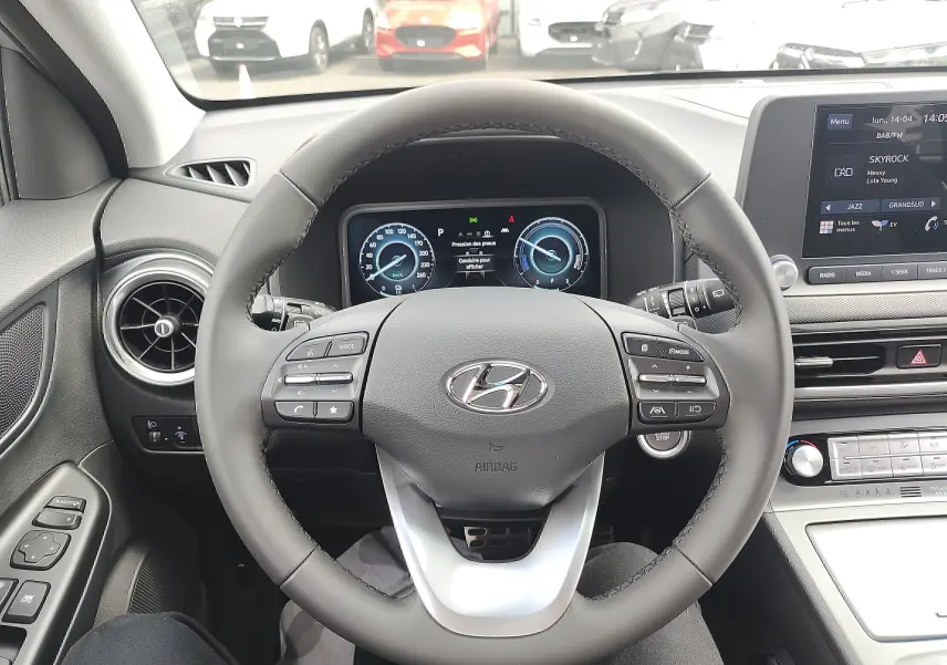 Vue intérieure centrée sur le volant cuir et tableau de bord numérique du Hyundai Kona Electric gris métallisé 2025.
