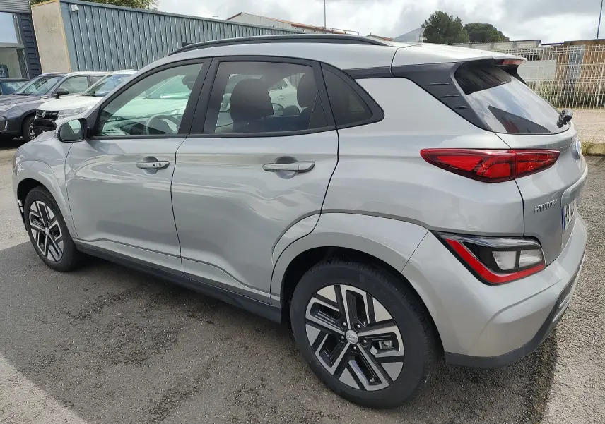 Vue 3/4 arrière côté gauche d'un Hyundai Kona électrique gris métallisé avec jantes alliage et vitres surteintées.