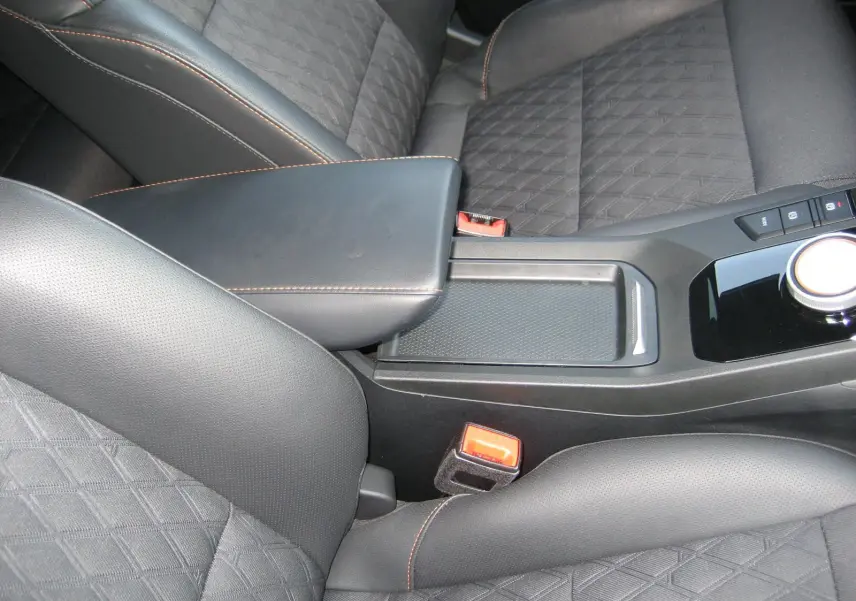 Gros plan sur l'accoudoir central noir et les sièges en cuir noir avec surpiqûres orange du MG3 1.5 HYBRID+ 2024.