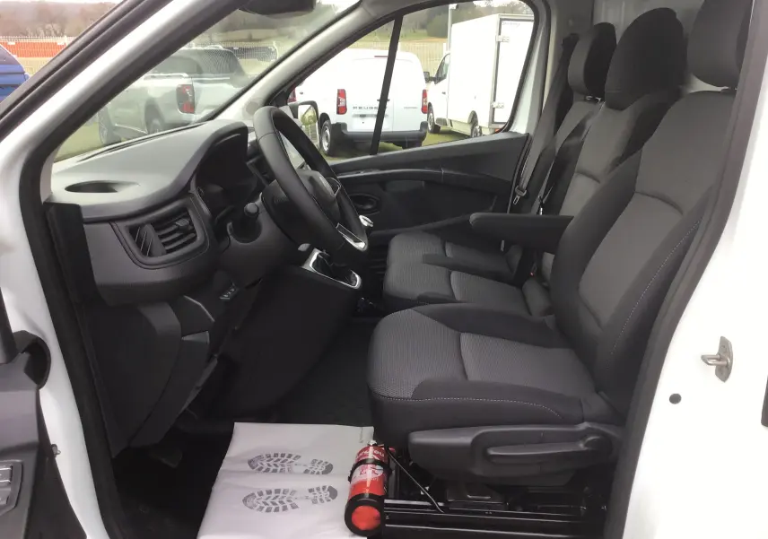 Vue intérieure côté conducteur du Renault Trafic Fourgon blanc 2025, montrant les sièges tissu gris et le volant.