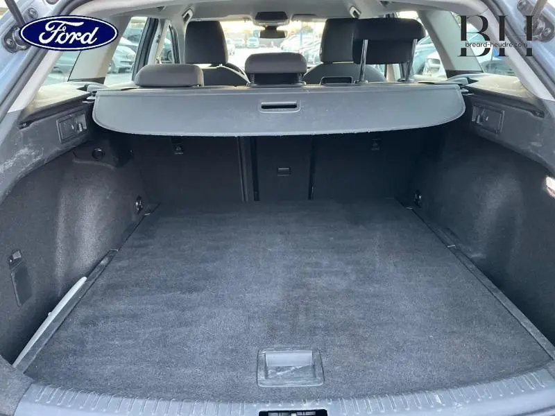 Coffre ouvert vu de l'arrière d'un SEAT LEON ST gris urbain métal, avec cache-bagages et banquette arrière noire.