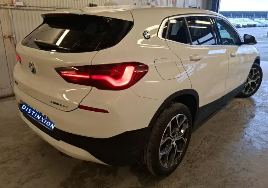 Vue 3/4 arrière droite d'un BMW X2 blanc avec jantes alliage 18'' et feux arrière allumés dans un garage.