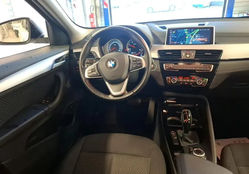 Vue intérieure avant du BMW X2 avec tableau de bord noir, volant multifonction et écran de navigation central.