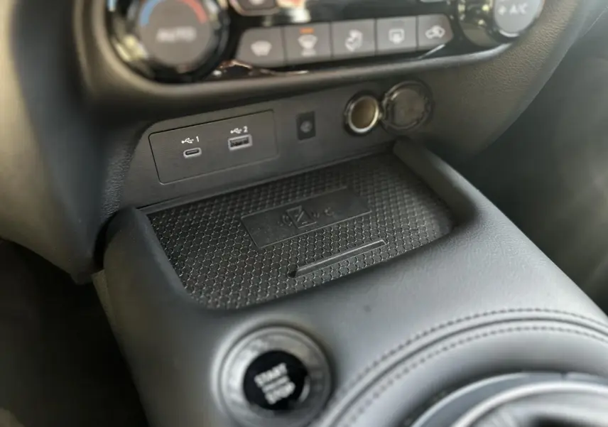 Gros plan sur la console centrale noire du Nissan Juke 2025, montrant le bouton Start/Stop et les ports USB avec chargeur sans fil.