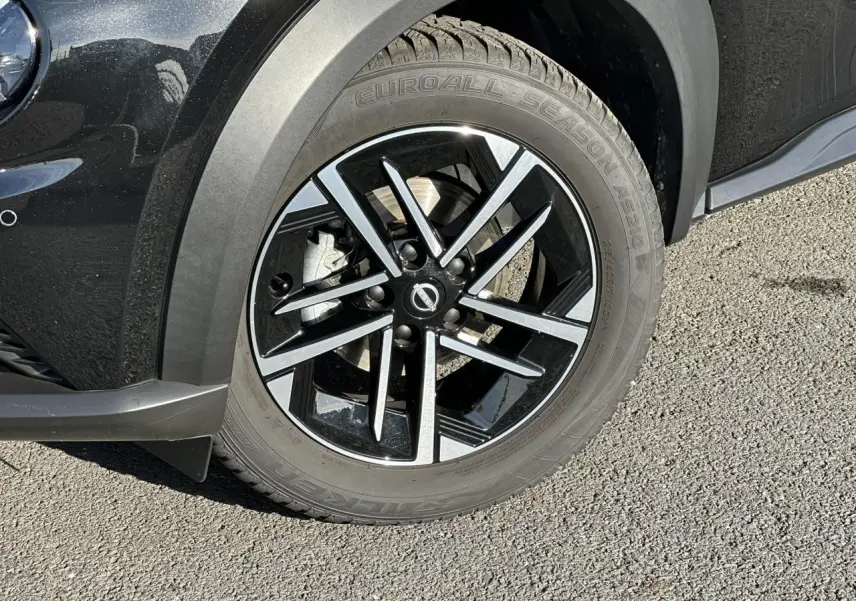 Gros plan sur la roue avant gauche noire du Nissan Juke 2025 avec jante alliage diamantée et pneu Euroall Season.