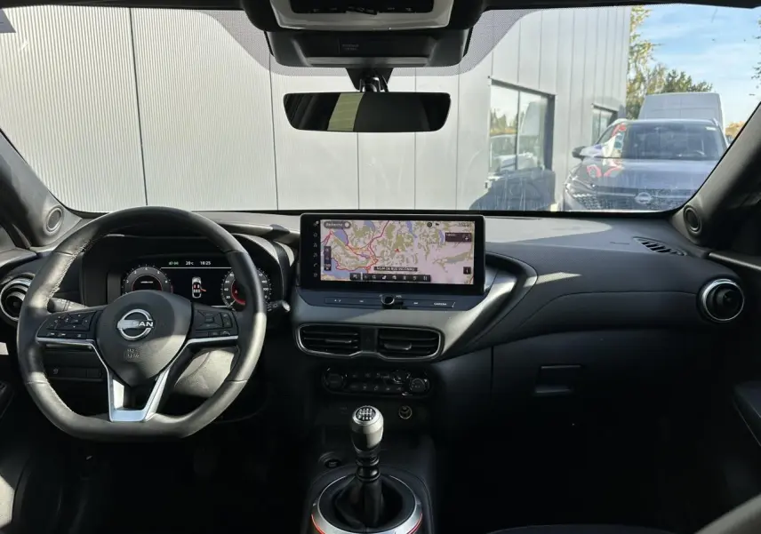 Vue intérieure avant du Nissan Juke noir 2025, mettant en valeur le volant, le combiné digital et l'écran tactile central.