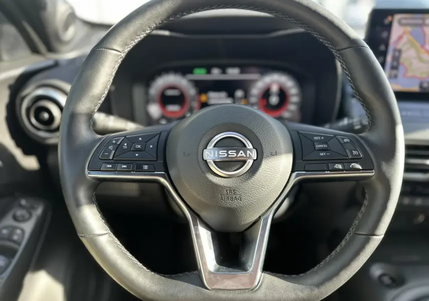 Vue rapprochée du volant en cuir noir du Nissan Juke 2025 avec commandes intégrées et tableau de bord digital flou.