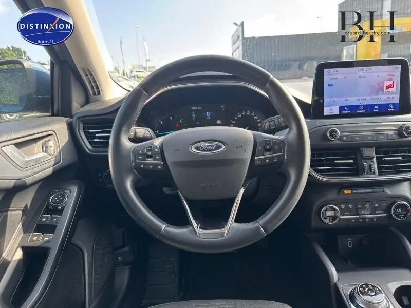 Vue intérieure centrée sur le volant cuir multifonction d'une Ford Focus bleu azur métallisé, avec écran tactile et commandes au tableau de bord