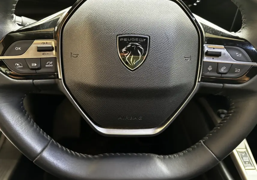 Gros plan sur le volant cuir noir de la Peugeot 308 PureTech 110 S&S ACTIVE PACK avec commandes multifonctions intégrées.