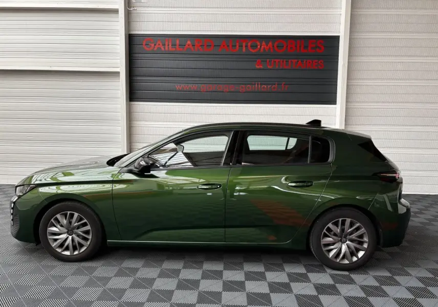 Profil côté gauche d'une Peugeot 308 vert foncé 2022 garée en intérieur avec jantes alliage et rétroviseurs noirs.