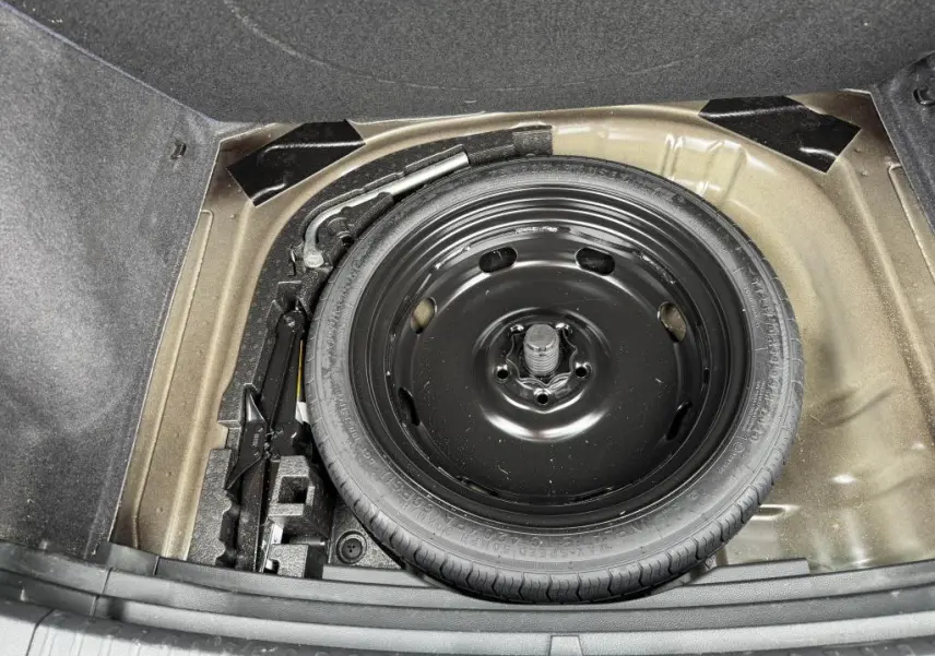 Roue de secours noire et outils de bord dans le coffre du SEAT Ateca 2023, vue plongeante sur l'espace de rangement.