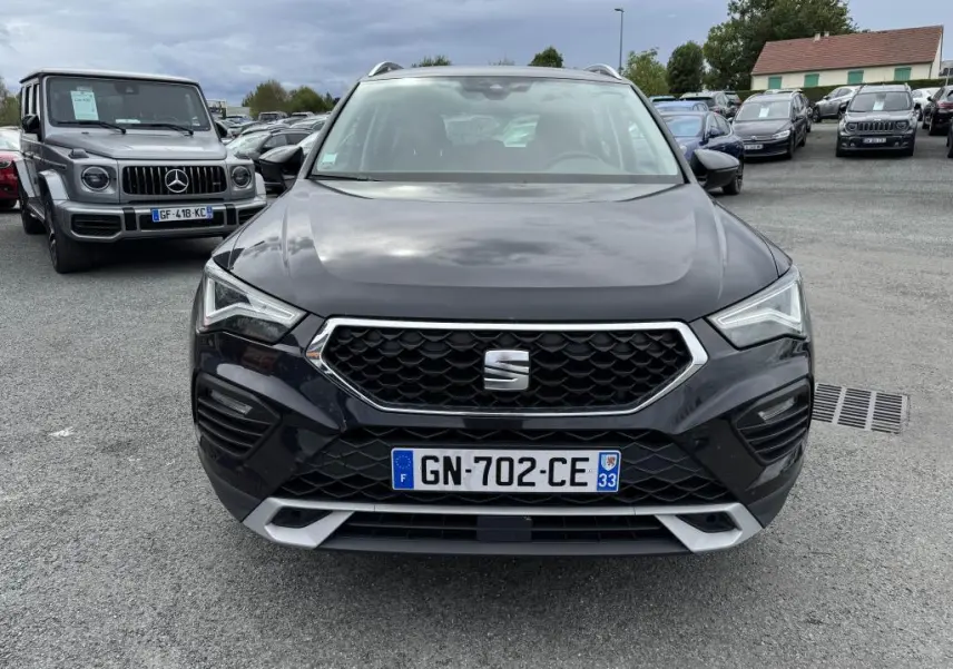 Vue frontale d'un SEAT Ateca noir métallisé avec calandre hexagonale et phares LED, sur un parking extérieur.
