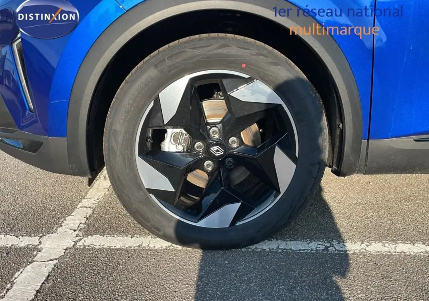 Gros plan sur la roue avant gauche du Renault Captur bleu Iron Metal avec jante noire et grise au design étoilé.