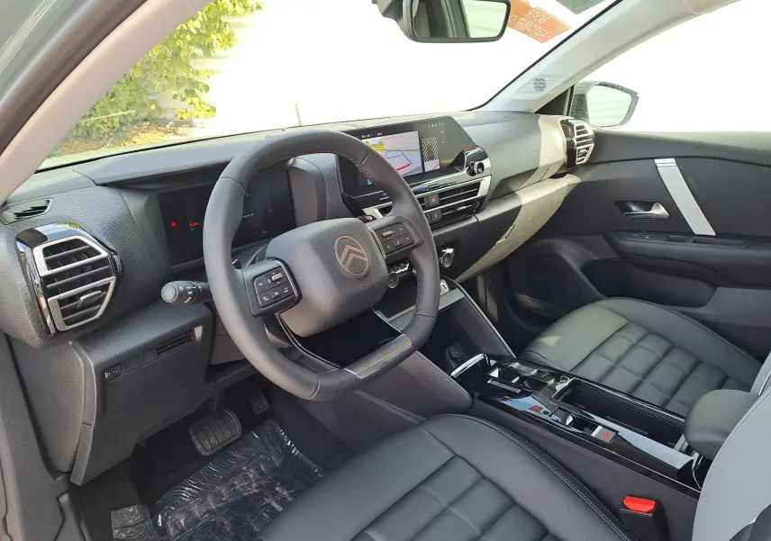 Vue intérieure côté conducteur de la Citroën C4 hybride 2025, avec tableau de bord moderne et sièges en cuir noir.